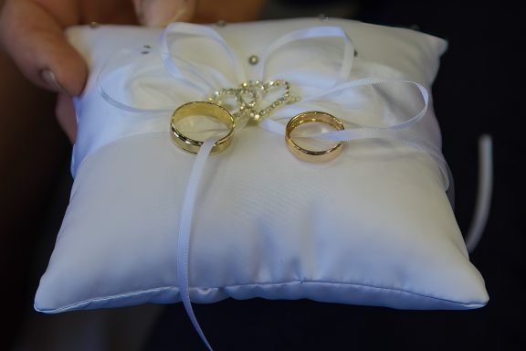 White cushion adorned with rings and delicate ribbons, often used in wedding ceremonies.