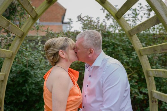Couple sharing a kiss under an archway surrounded by greenery.